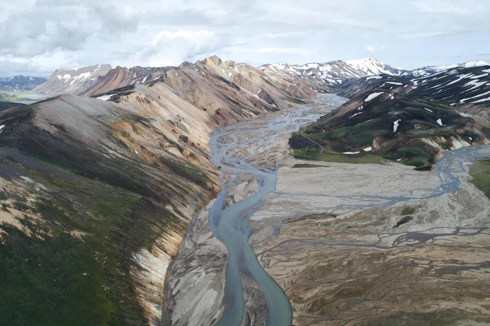 Glacial meltwater river braiding across a volcanic ash plain in the Landmannalaugar Highlands, surrounded by rhyolite peaks formed by past Icelandic eruptions