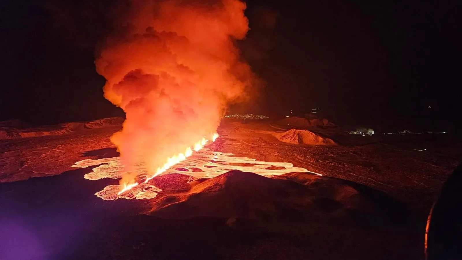 Lava fissure eruption at night on the Reykjanes Peninsula with glowing orange flows across dark basalt field, Iceland